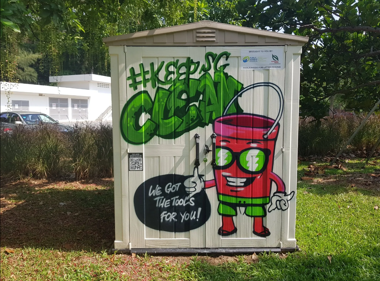 A CleanPod unit decorated with vibrant graffiti-style artwork, featuring the hashtag #KeepSGClean and a cartoon character holding cleanup tools with the words 'We Got The Tools For You!', situated outdoors on a grassy area.